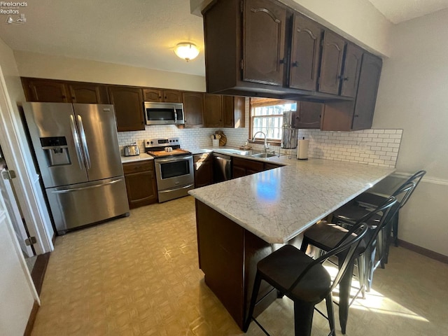 kitchen featuring sink, backsplash, kitchen peninsula, a breakfast bar area, and appliances with stainless steel finishes