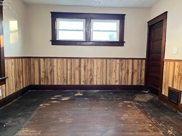 empty room with dark hardwood / wood-style floors, a healthy amount of sunlight, a textured ceiling, and wooden walls