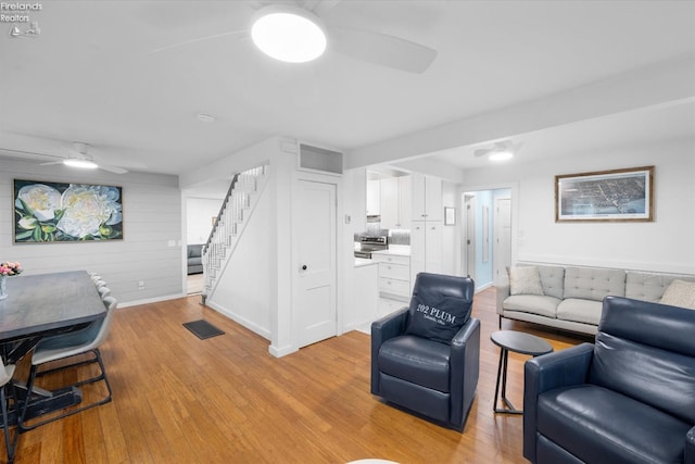 living room with ceiling fan, wood walls, and light wood-type flooring