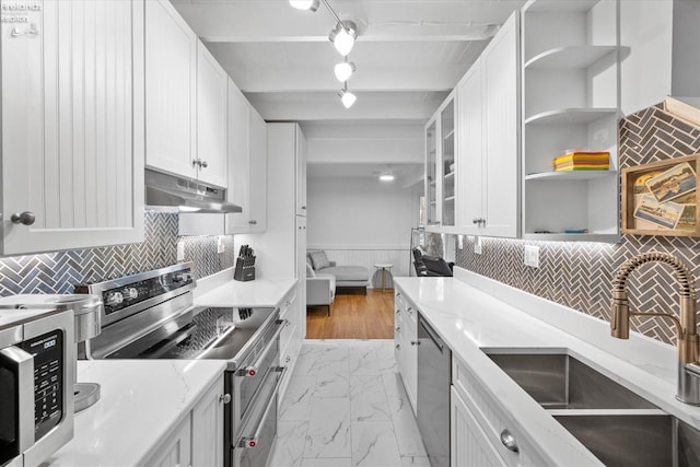 kitchen with beam ceiling, white cabinetry, sink, light stone countertops, and appliances with stainless steel finishes