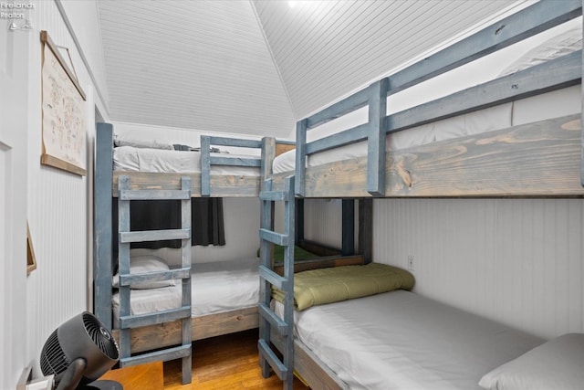 bedroom with hardwood / wood-style floors, lofted ceiling, and wood walls