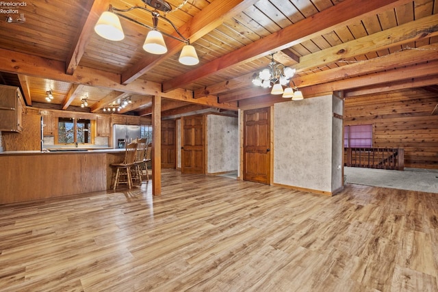 unfurnished living room with beamed ceiling, a notable chandelier, wood walls, and light hardwood / wood-style flooring