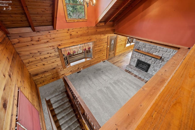 unfurnished living room with wood walls, wooden ceiling, a stone fireplace, vaulted ceiling with beams, and wood-type flooring