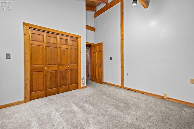 unfurnished bedroom with carpet, beam ceiling, high vaulted ceiling, and a closet