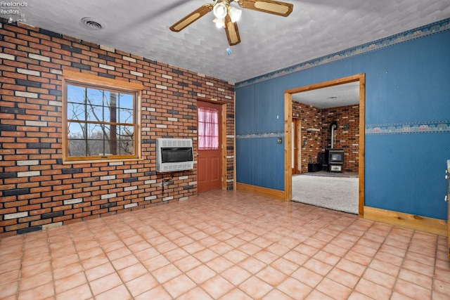 unfurnished living room featuring a textured ceiling, heating unit, a wood stove, and brick wall