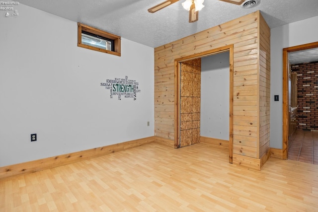 unfurnished bedroom with hardwood / wood-style floors, ceiling fan, a textured ceiling, and wooden walls