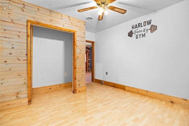 bedroom featuring ceiling fan, wood-type flooring, a textured ceiling, and wooden walls