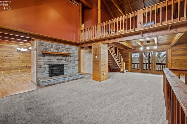 unfurnished living room featuring carpet, wooden ceiling, beamed ceiling, a fireplace, and wood walls