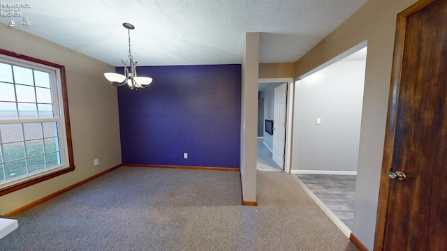 carpeted spare room with a wealth of natural light, a textured ceiling, and an inviting chandelier