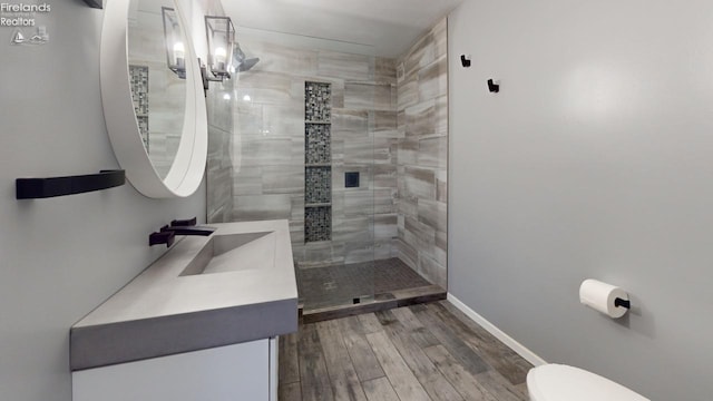 bathroom with a tile shower, vanity, wood-type flooring, and toilet