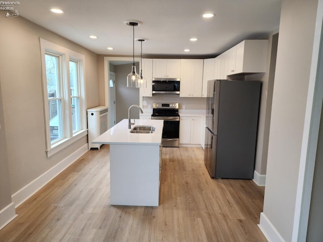 kitchen with appliances with stainless steel finishes, a kitchen island with sink, sink, pendant lighting, and white cabinets