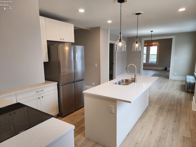 kitchen featuring white cabinets, stainless steel fridge, an island with sink, and sink