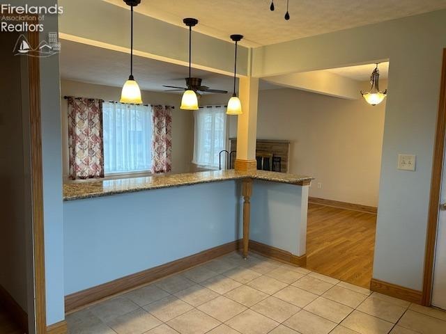 kitchen with pendant lighting, stone counters, light hardwood / wood-style flooring, ceiling fan, and kitchen peninsula