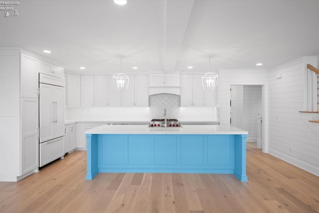 kitchen featuring hanging light fixtures, paneled refrigerator, light hardwood / wood-style flooring, a center island with sink, and white cabinets