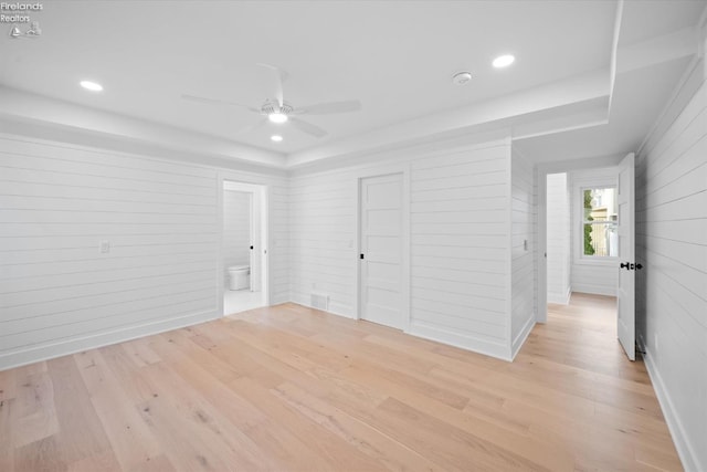 unfurnished bedroom featuring ceiling fan, light wood-type flooring, and wooden walls