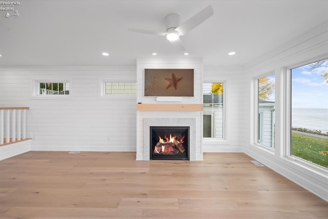 unfurnished living room featuring a fireplace, light hardwood / wood-style floors, a wealth of natural light, and a water view