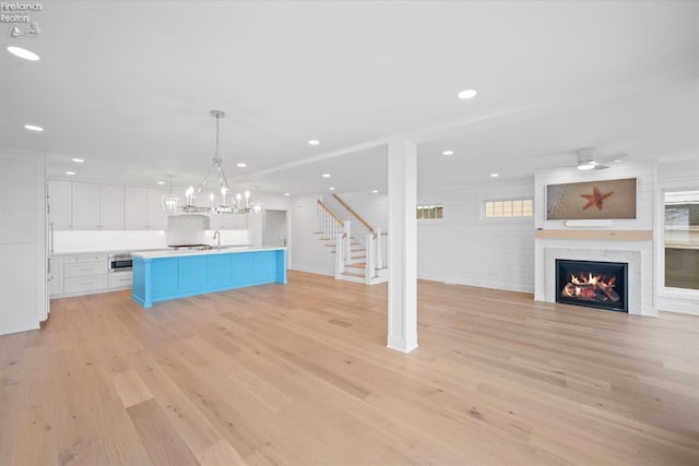 kitchen featuring light wood-type flooring, a large fireplace, a kitchen island with sink, white cabinets, and hanging light fixtures