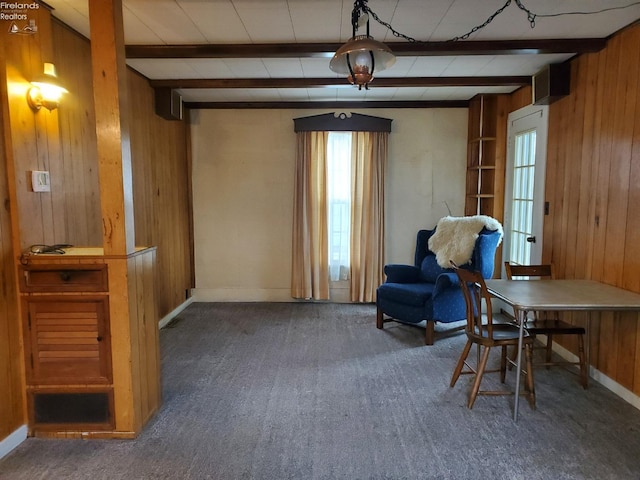 sitting room with dark colored carpet, beam ceiling, and wood walls