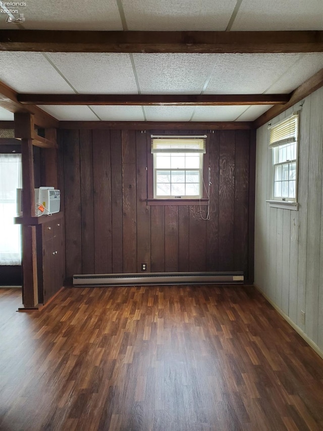 interior space with a drop ceiling, dark hardwood / wood-style flooring, wooden walls, and a baseboard radiator