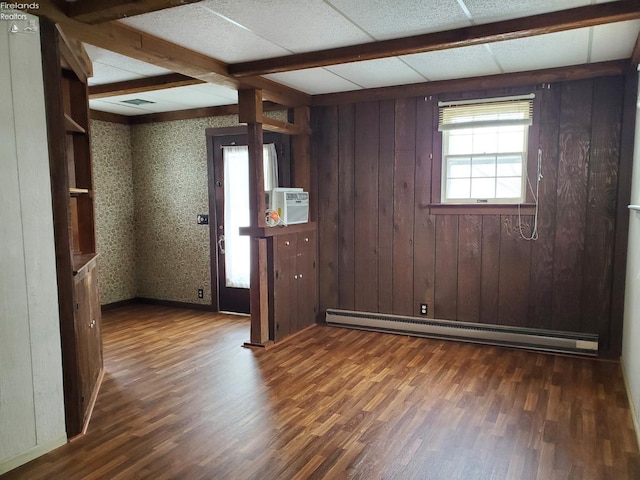 empty room featuring wood walls, dark wood-type flooring, and a baseboard heating unit