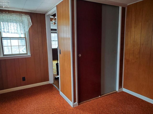 unfurnished bedroom with carpet flooring, wood walls, and a closet