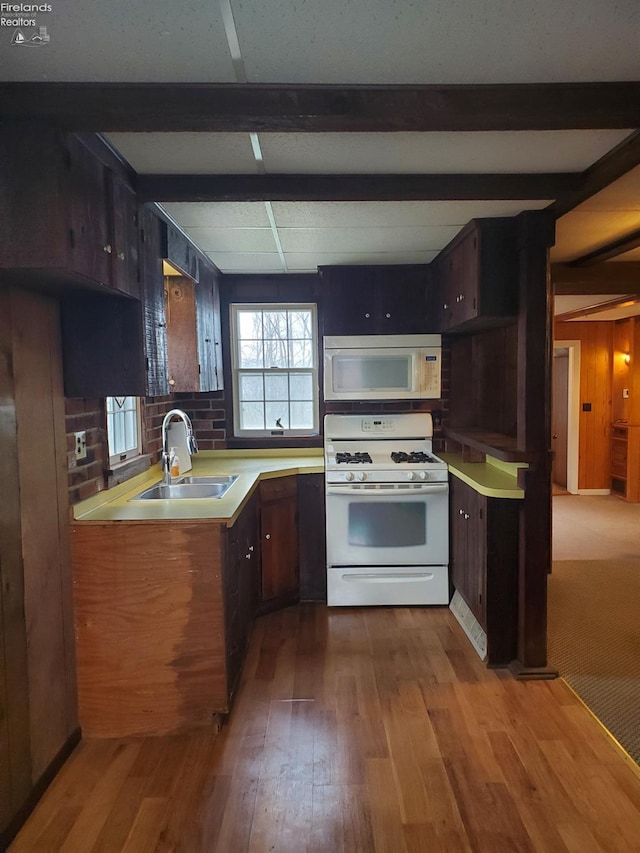 kitchen with sink, light hardwood / wood-style flooring, white appliances, wooden walls, and dark brown cabinets