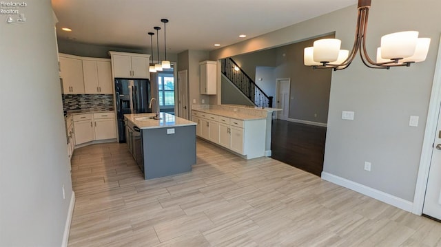 kitchen with an inviting chandelier, an island with sink, light hardwood / wood-style floors, pendant lighting, and white cabinets