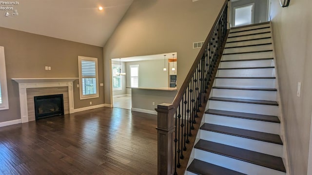 stairs with a tile fireplace, hardwood / wood-style floors, high vaulted ceiling, and a notable chandelier