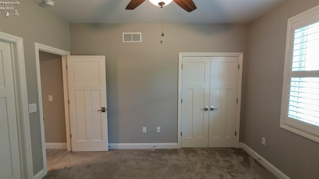 unfurnished bedroom with dark colored carpet, a closet, and ceiling fan