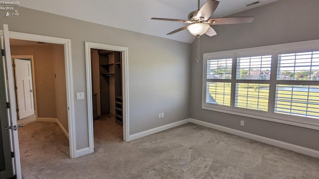 unfurnished bedroom with a closet, a walk in closet, light colored carpet, and ceiling fan