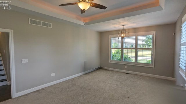 spare room with a raised ceiling, light colored carpet, and ceiling fan with notable chandelier