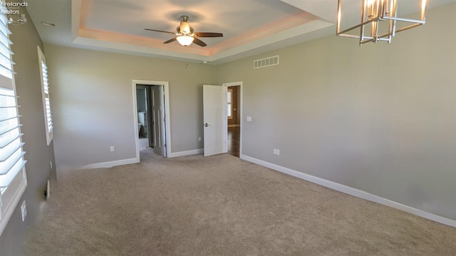 unfurnished room with a raised ceiling, carpet floors, and ceiling fan with notable chandelier