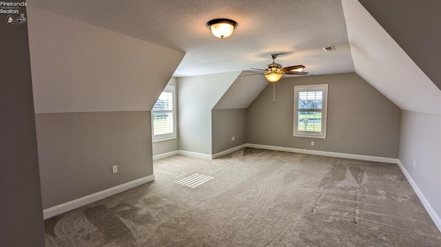 additional living space featuring vaulted ceiling, ceiling fan, light colored carpet, and a textured ceiling