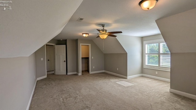 additional living space featuring a textured ceiling, light colored carpet, ceiling fan, and lofted ceiling