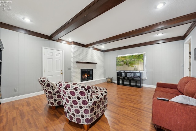 living room with crown molding, a fireplace, beamed ceiling, and wood-type flooring