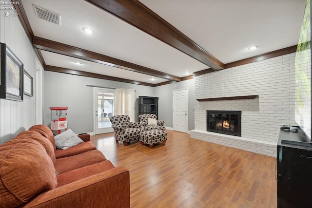 living room with a brick fireplace, crown molding, beamed ceiling, and light wood-type flooring