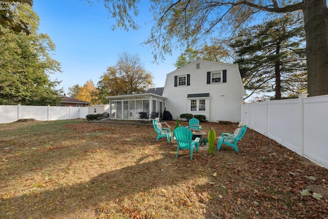 back of property with a lawn, a sunroom, and an outdoor fire pit