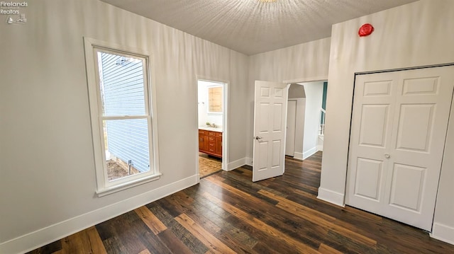 unfurnished bedroom with ensuite bath, dark wood-type flooring, and a textured ceiling