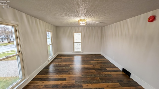 empty room with dark hardwood / wood-style flooring, a textured ceiling, and a wealth of natural light