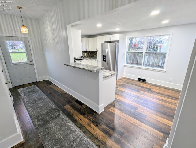 kitchen with kitchen peninsula, stainless steel fridge, light stone counters, decorative light fixtures, and white cabinetry