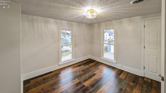 empty room featuring a textured ceiling, dark hardwood / wood-style floors, and a healthy amount of sunlight