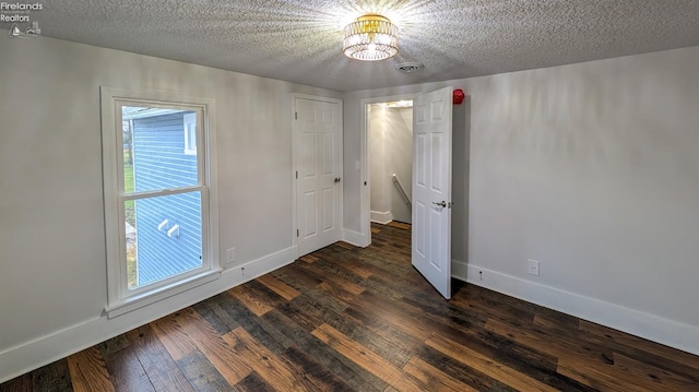 unfurnished room featuring a chandelier, a textured ceiling, and dark hardwood / wood-style flooring