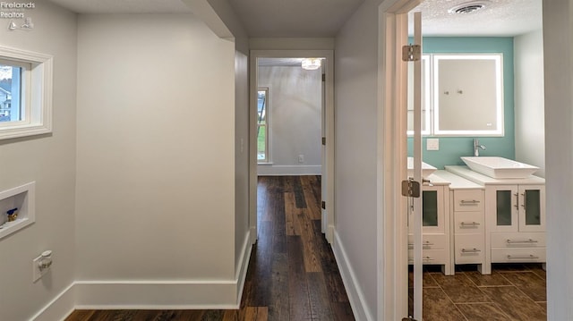 hallway with a textured ceiling, dark hardwood / wood-style flooring, and sink