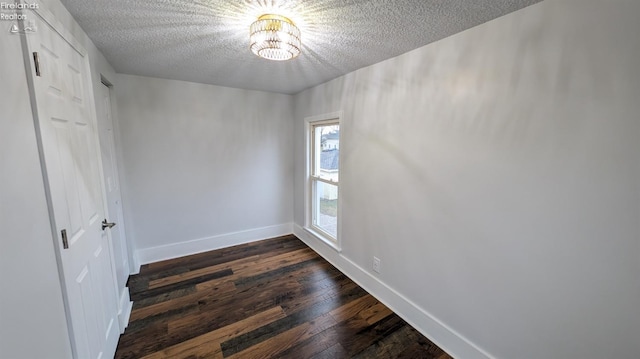 empty room with a textured ceiling, an inviting chandelier, and dark wood-type flooring