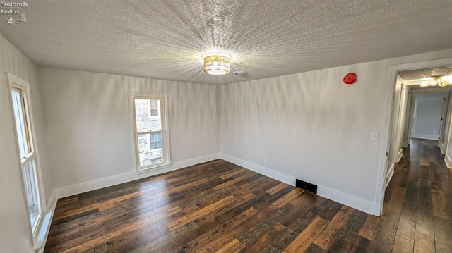 empty room featuring a textured ceiling, a chandelier, and dark hardwood / wood-style floors