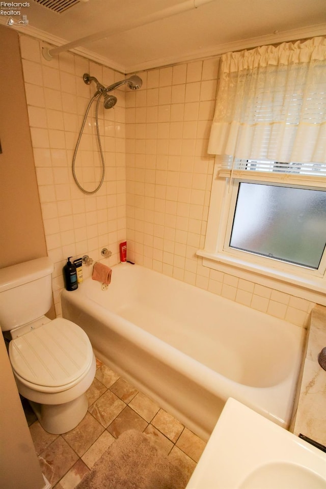 bathroom with tile patterned flooring, crown molding, toilet, and tiled shower / bath