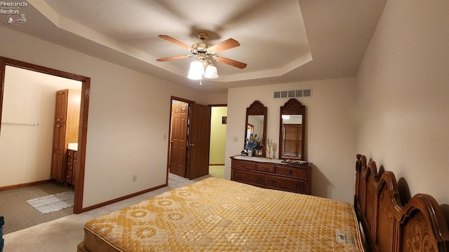 bedroom with a tray ceiling, ensuite bathroom, ceiling fan, and light colored carpet