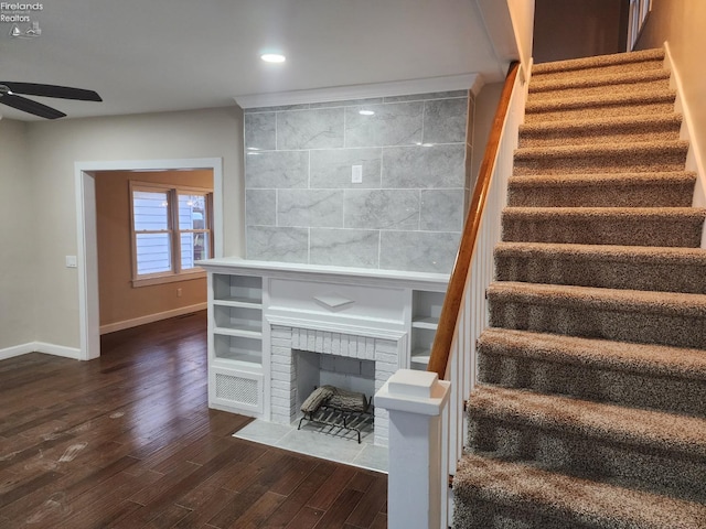 stairs with ceiling fan, hardwood / wood-style floors, and a brick fireplace