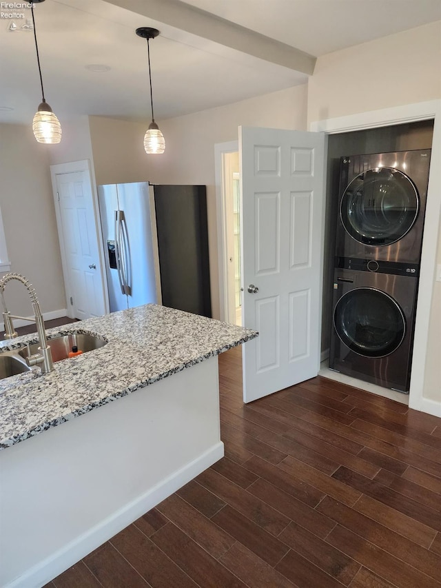 kitchen with light stone countertops, sink, dark hardwood / wood-style flooring, pendant lighting, and stacked washer / drying machine