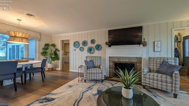 living room with a stone fireplace, crown molding, and hardwood / wood-style floors